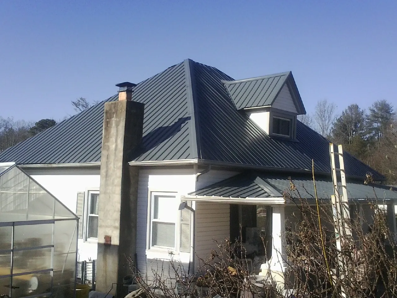 Dark blue standing seam metal roof on a white farmhouse with dormer — Slate & Tile Roof Repair by Roofing Brothers in Gilmanton