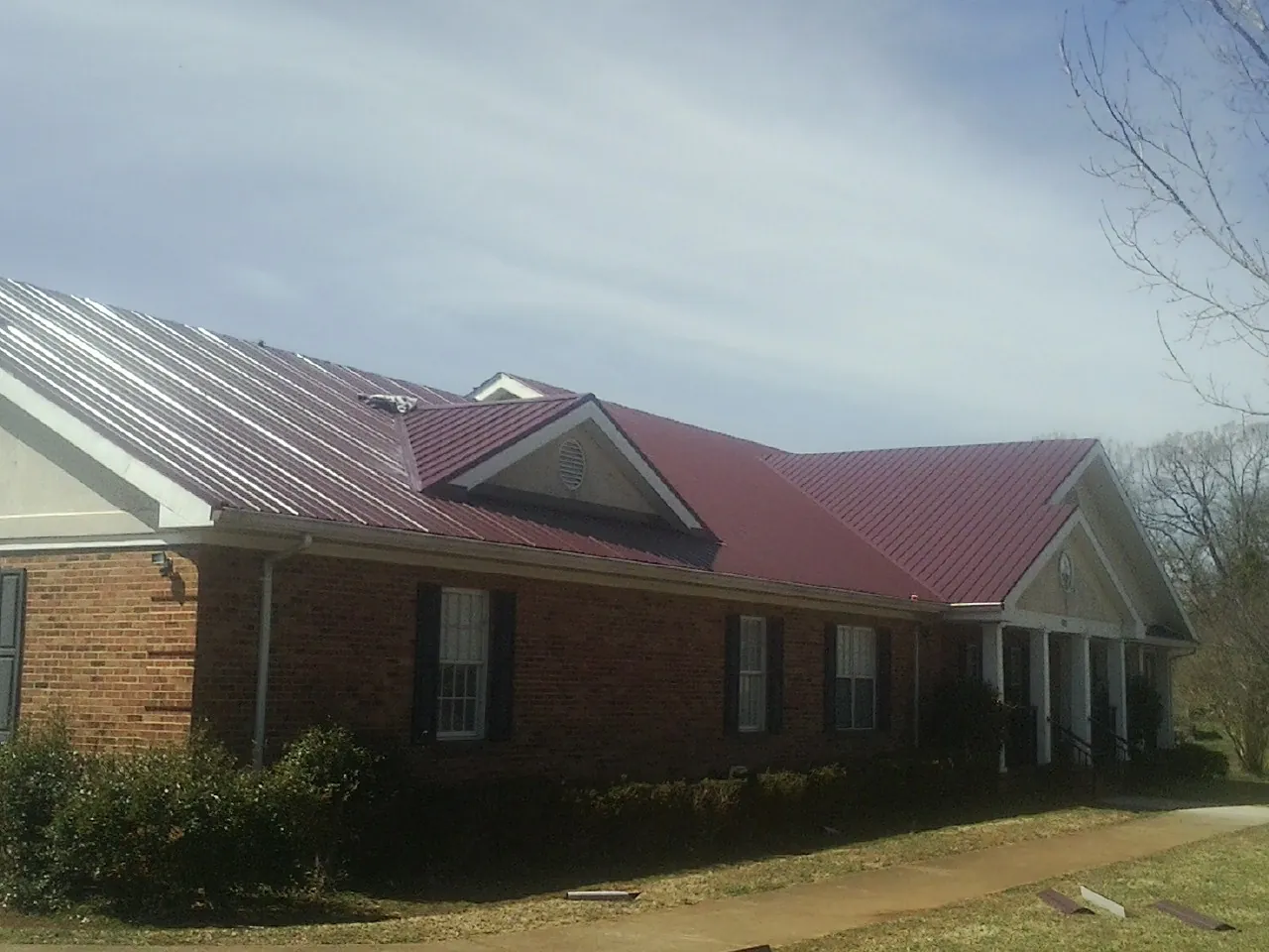 Red metal roof with gabled entries on a long brick building, from a Hail Damage Roof Repair job in Gilmanton