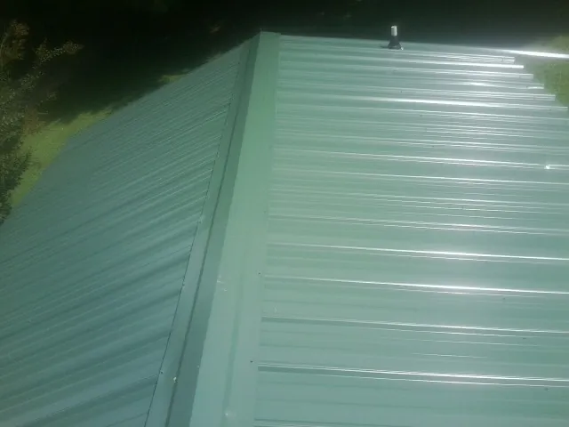 New green metal panels meeting at the ridge of a roof — Flat Roof Repair work by our crew in Gilmanton