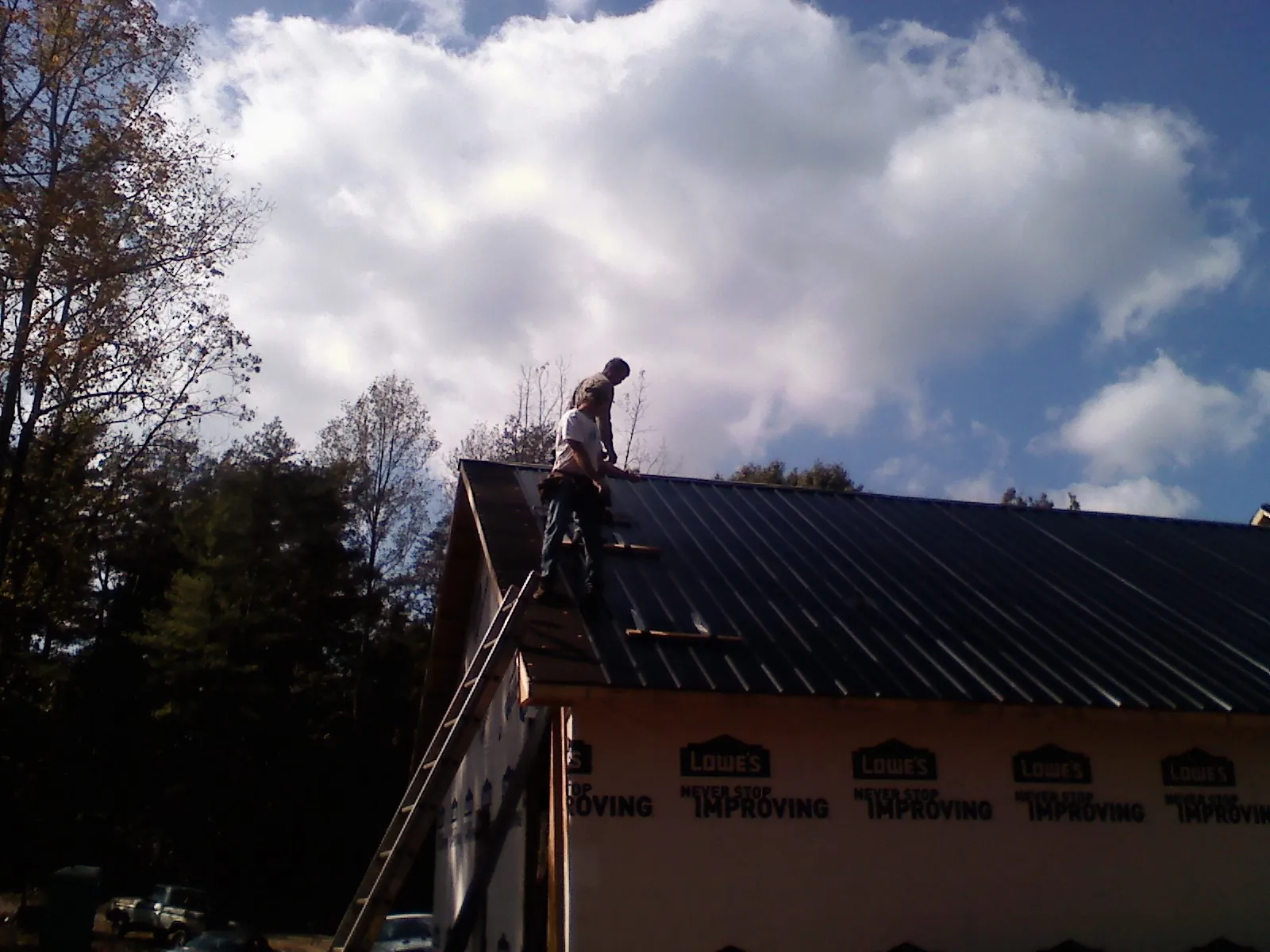Roofer fastening dark metal panels high against a cloudy sky, from a Roof Inspection job in Gilmanton