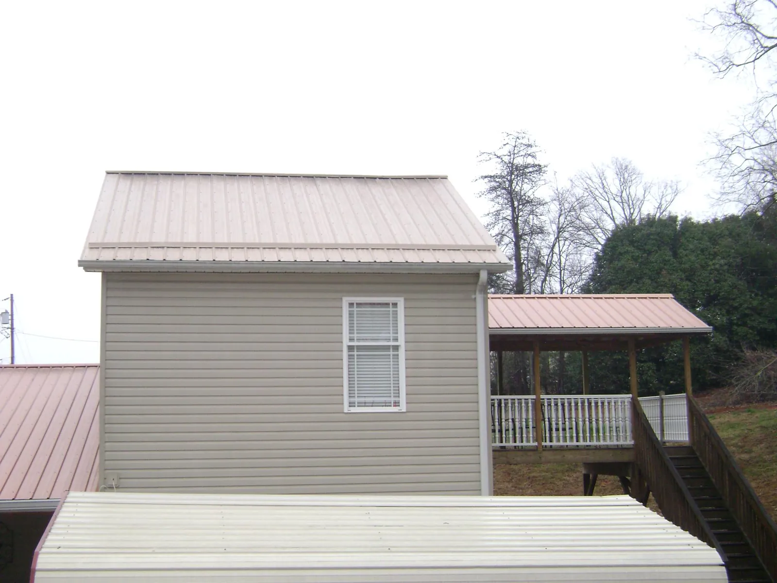 Tan metal roofs on a two story addition and attached porch, from a Roof Replacement job in Gilmanton