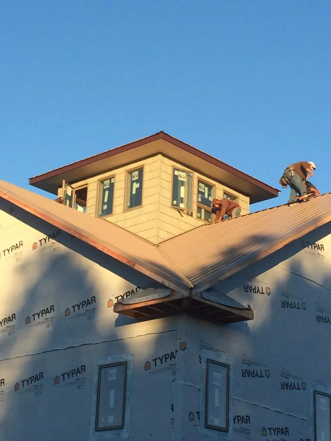 Roofers working around a rooftop cupola on a new metal roof at sunset — Roof Waterproofing in Gilmanton by Roofing Brothers